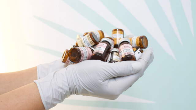 Gloved hands holding a jumbled stack of medicine bottles.