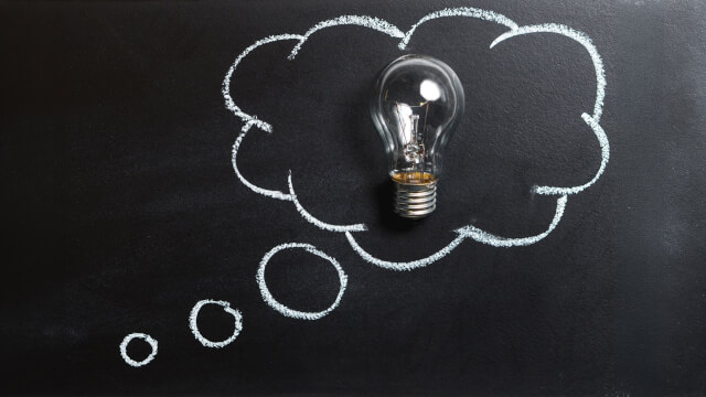 A lightbulb resting on a blackboard, surrounded by a cloud drawn in chalk, as if a thought bubble